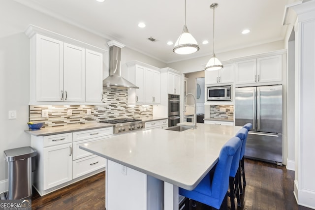 kitchen featuring built in appliances, a kitchen island with sink, wall chimney exhaust hood, white cabinets, and backsplash
