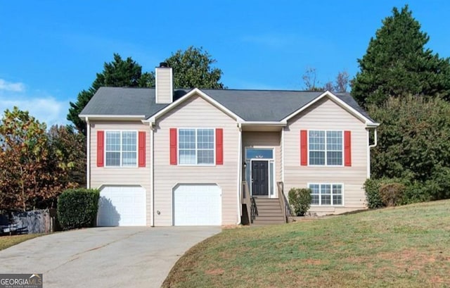 raised ranch with an attached garage, a front yard, entry steps, a chimney, and driveway