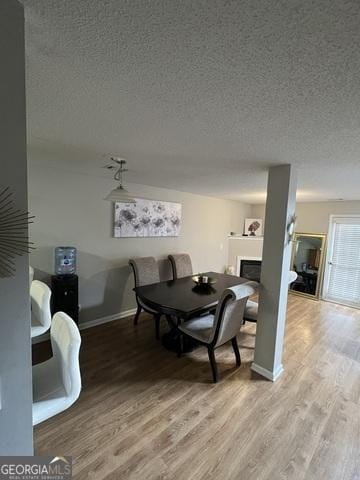 dining space featuring light wood-style floors, a textured ceiling, baseboards, and a fireplace