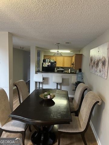 dining room featuring baseboards, a textured ceiling, and light wood finished floors