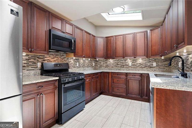 kitchen featuring a sink, stainless steel appliances, a skylight, tasteful backsplash, and light stone counters