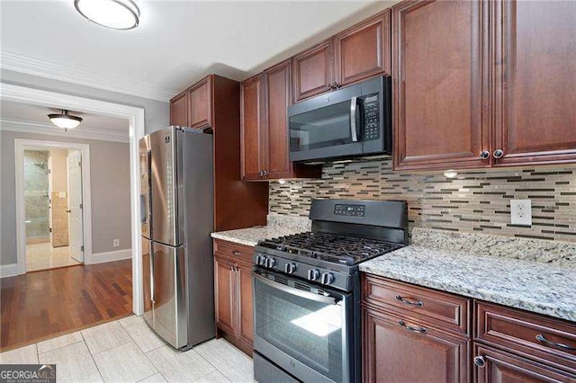 kitchen featuring baseboards, light stone counters, ornamental molding, decorative backsplash, and stainless steel appliances