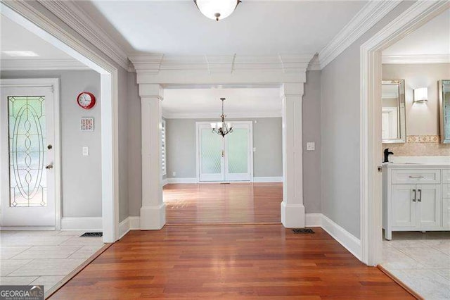 entrance foyer featuring an inviting chandelier, light wood-style flooring, baseboards, and ornate columns