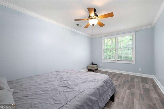 bedroom featuring wood finished floors, a ceiling fan, crown molding, visible vents, and baseboards