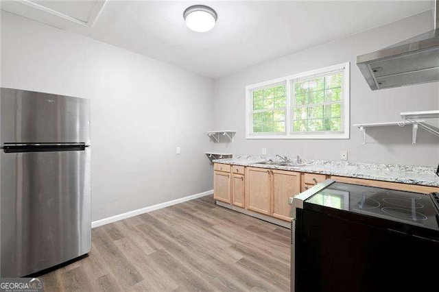 kitchen with freestanding refrigerator, light brown cabinetry, a sink, wall chimney exhaust hood, and light wood-style floors