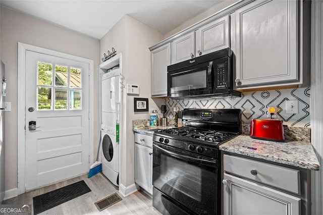 1941 Headland Dr, East Point, GA 30344 - kitchen with visible vents, stacked washer and clothes dryer, light wood-style floors, backsplash, and black appliances