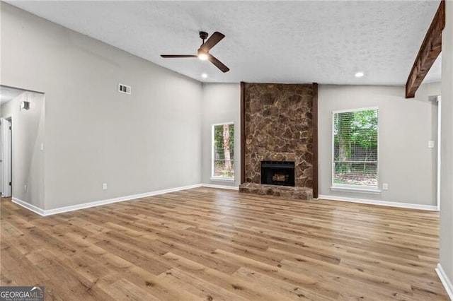 unfurnished living room with light wood-style flooring, lofted ceiling, a textured ceiling, a stone fireplace, and ceiling fan