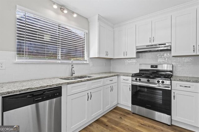 kitchen featuring appliances with stainless steel finishes, under cabinet range hood, a sink, white cabinets, and healthy amount of natural light