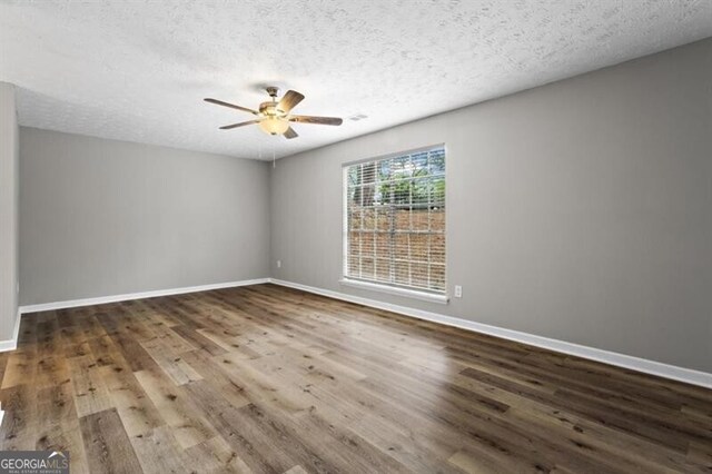 empty room with a ceiling fan, wood finished floors, baseboards, and a textured ceiling