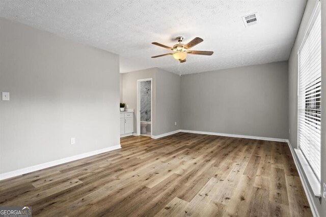 unfurnished room with healthy amount of natural light, wood finished floors, a ceiling fan, and a textured ceiling