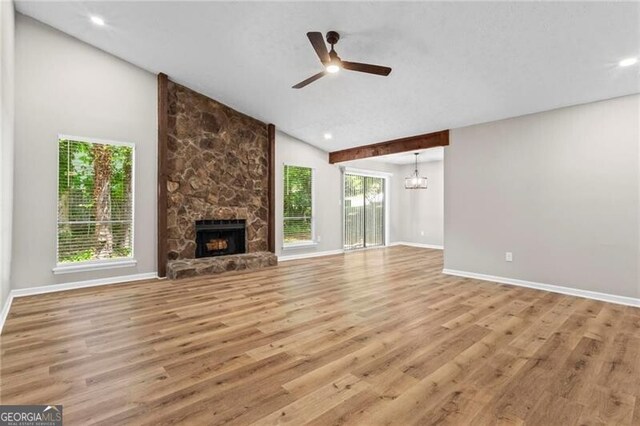 unfurnished living room with wood finished floors, baseboards, a stone fireplace, a textured ceiling, and high vaulted ceiling