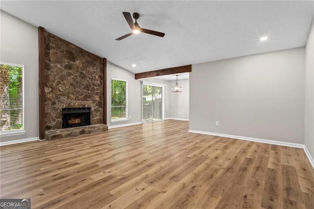 unfurnished living room with wood finished floors, a stone fireplace, a ceiling fan, baseboards, and lofted ceiling