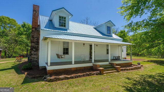 view of front of house with a porch, a chimney, metal roof, and a front lawn