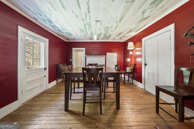 dining area featuring wood-type flooring, wood walls, and ornamental molding