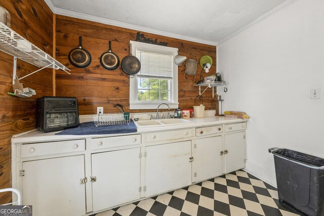 kitchen featuring ornamental molding, light floors, wooden walls, white cabinetry, and a sink