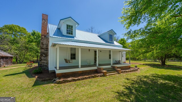 rear view of house with a chimney, a yard, a porch, and metal roof