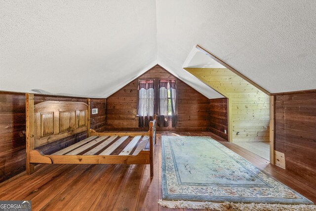 bonus room with a textured ceiling, wood walls, and hardwood / wood-style flooring