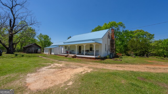 view of front of house with covered porch, driveway, a chimney, central AC, and a front lawn