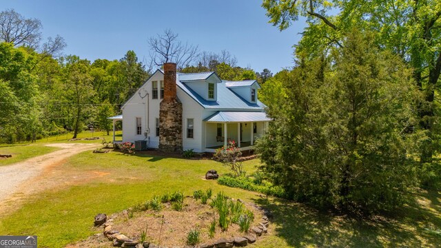 view of home's exterior with covered porch, driveway, a chimney, metal roof, and a yard