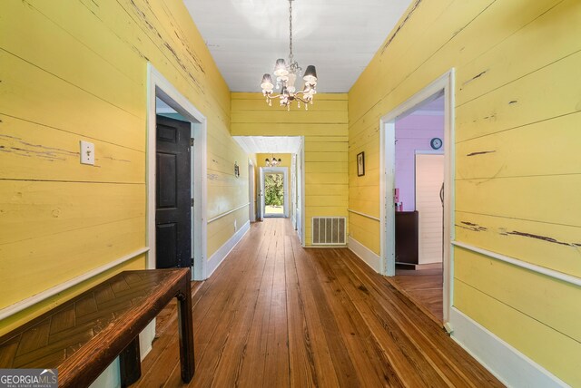 corridor featuring visible vents, wood walls, a notable chandelier, and hardwood / wood-style flooring