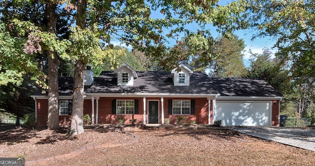 cape cod home featuring brick siding, a garage, driveway, and a porch