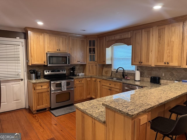 kitchen featuring a peninsula, a breakfast bar, tasteful backsplash, a sink, and appliances with stainless steel finishes