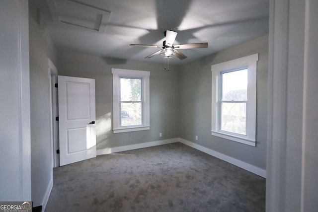 empty room with carpet floors, attic access, baseboards, and ceiling fan