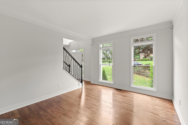unfurnished living room with baseboards, ornamental molding, wood finished floors, and stairway