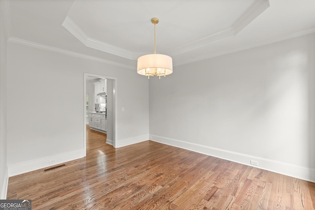 spare room featuring wood finished floors, a tray ceiling, visible vents, a chandelier, and ornamental molding