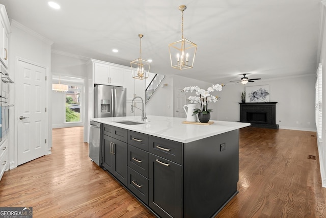 kitchen featuring a sink, stainless steel appliances, a fireplace, white cabinetry, and light countertops