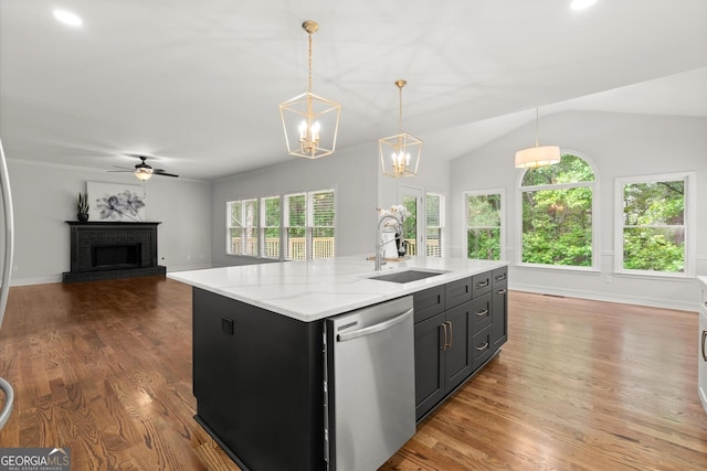 kitchen with a fireplace, a center island with sink, wood finished floors, dishwasher, and a sink