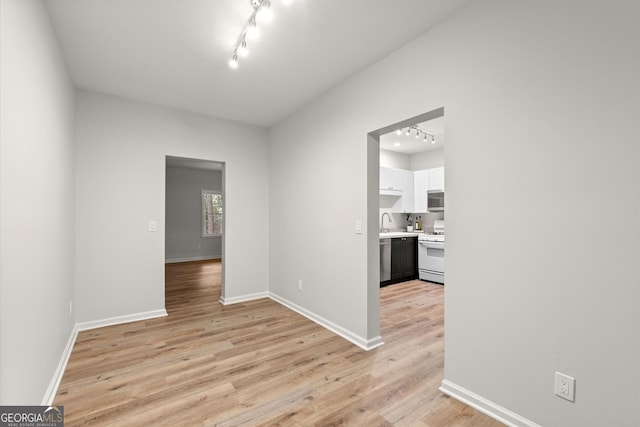 spare room featuring a sink, light wood finished floors, baseboards, and track lighting