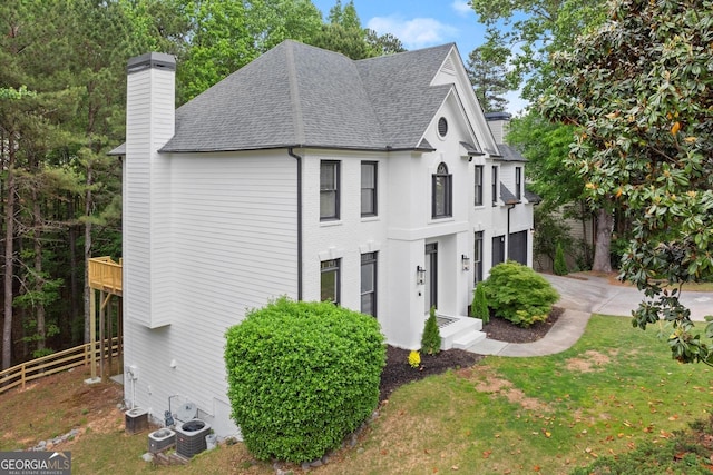view of side of home with an attached garage, fence, a chimney, a shingled roof, and a lawn