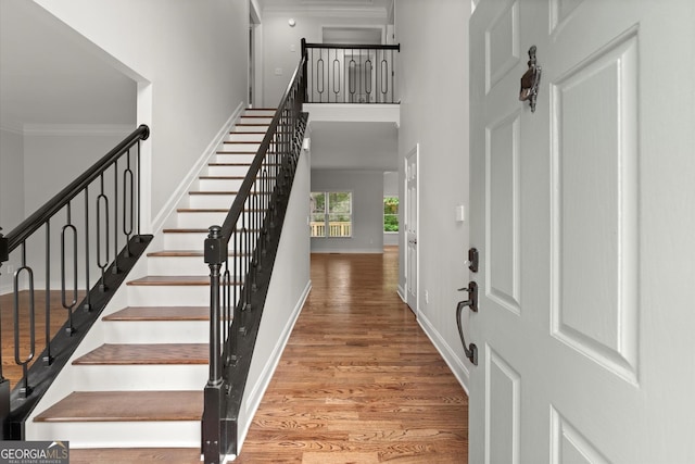 foyer entrance with baseboards, ornamental molding, stairs, and wood finished floors