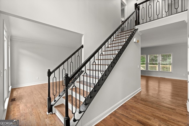 stairs with baseboards, visible vents, wood finished floors, and a high ceiling