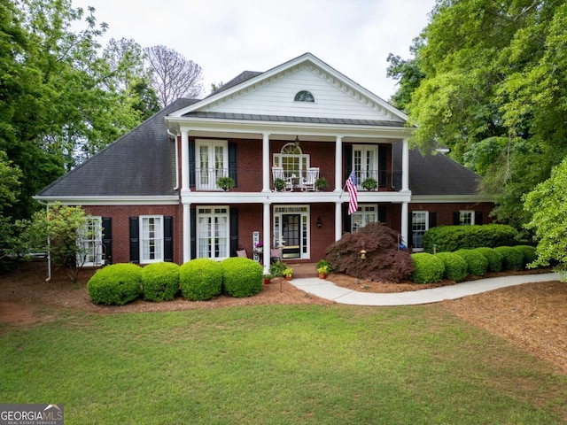 greek revival inspired property featuring a front lawn, a balcony, french doors, brick siding, and a porch