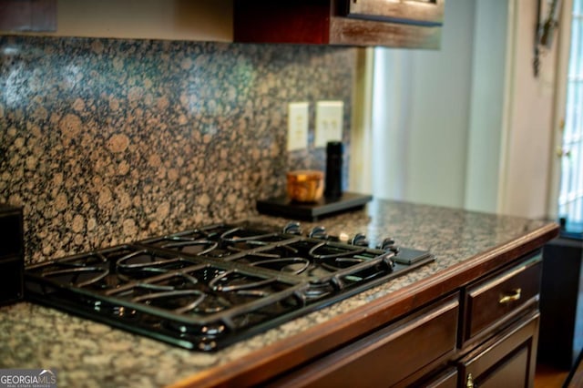 kitchen featuring decorative backsplash, dark brown cabinetry, black gas stovetop, and dark stone counters