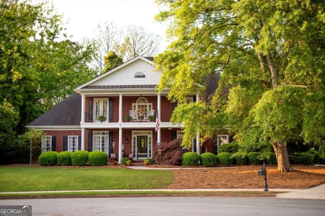 neoclassical home with brick siding, a balcony, and a front yard