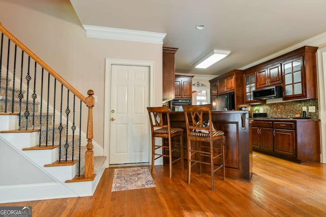 kitchen with crown molding, glass insert cabinets, light wood-style floors, and black appliances