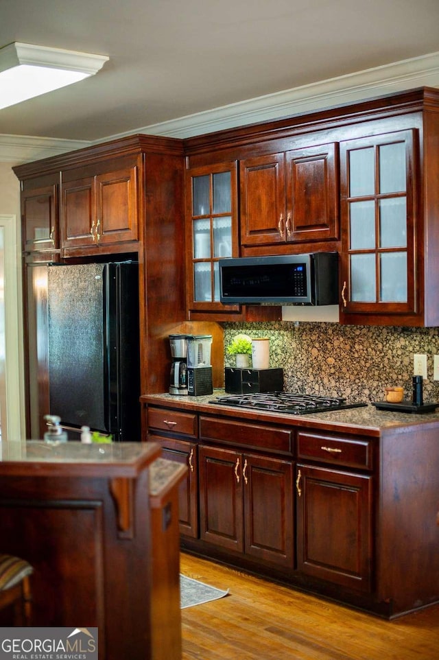 kitchen featuring ornamental molding, light wood finished floors, black appliances, and glass insert cabinets
