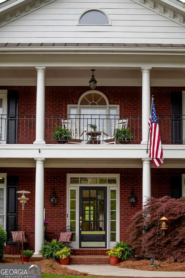 doorway to property with covered porch, brick siding, and a balcony