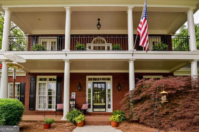 doorway to property featuring a porch, a balcony, and brick siding