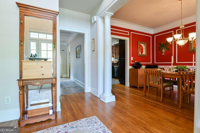 dining area with wood finished floors, baseboards, a notable chandelier, ornamental molding, and ornate columns