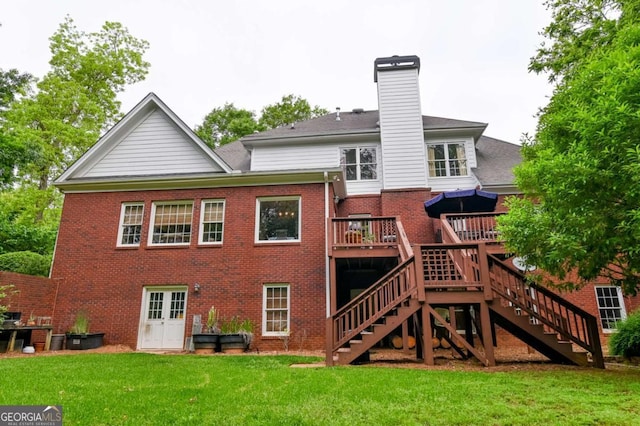 rear view of property with a wooden deck, a chimney, brick siding, stairs, and a yard