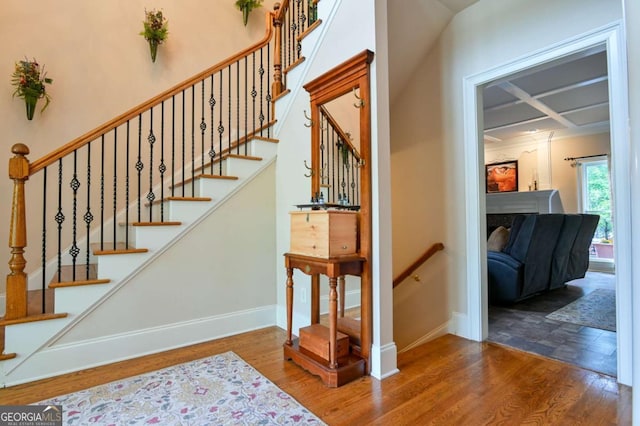 staircase featuring baseboards, coffered ceiling, and wood finished floors