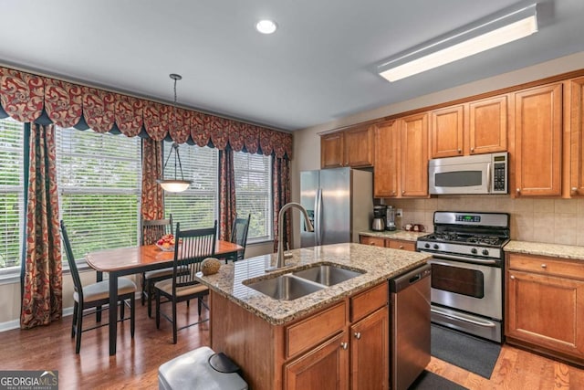 661 Village Field Ct NW, Suwanee, GA 30024 - kitchen featuring brown cabinetry, a kitchen island with sink, a sink, light wood finished floors, and appliances with stainless steel finishes