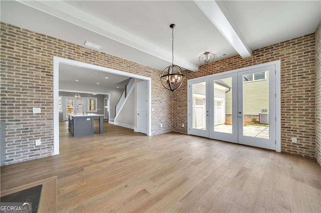 7235 Cordery Rd, Cumming, GA 30040 - interior space with a notable chandelier, brick wall, french doors, a wealth of natural light, and light wood-type flooring