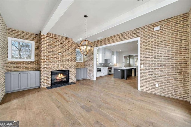 7235 Cordery Rd, Cumming, GA 30040 - unfurnished living room with brick wall, a brick fireplace, light wood-type flooring, beam ceiling, and an inviting chandelier