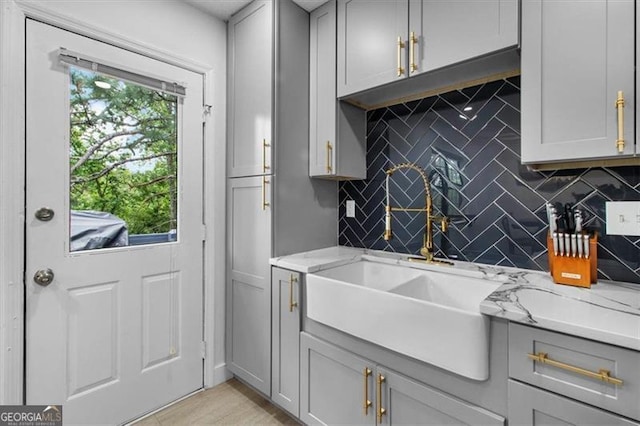 kitchen with gray cabinetry, tasteful backsplash, light stone countertops, and a sink