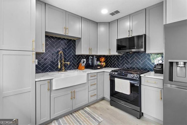 kitchen featuring gray cabinets, visible vents, appliances with stainless steel finishes, tasteful backsplash, and a sink